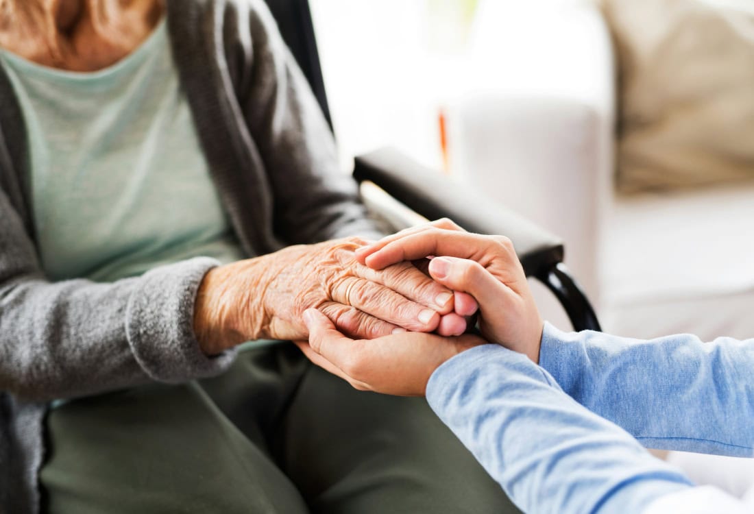 Zorgzame hand vasthouden tussen oudere en jongere persoon, emotionele steun en verbondenheid.