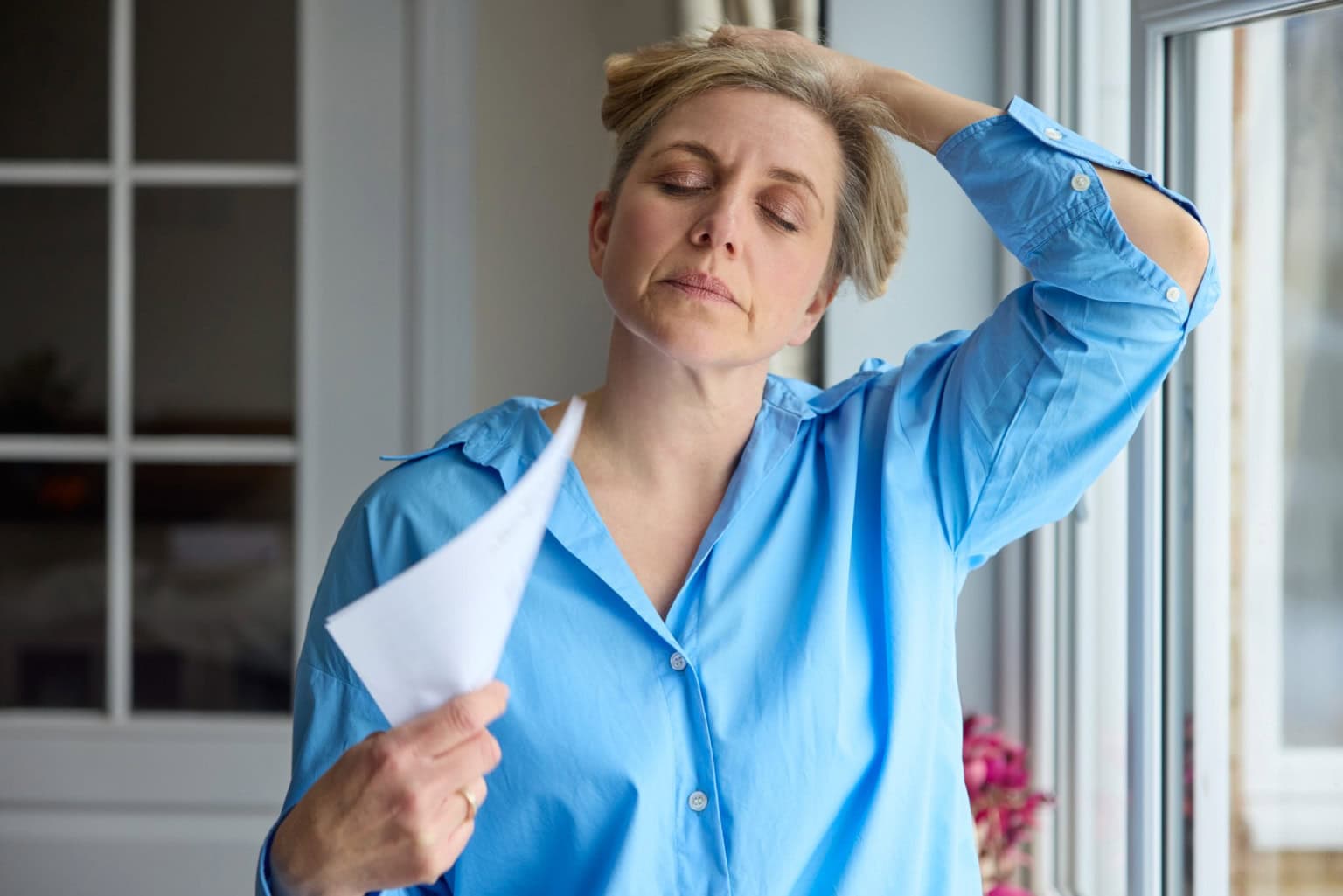 Vrouw met hoofdpijn houdt tissue en staat bij raam in huis.